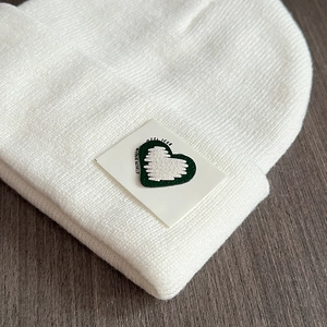 Detailed view of white knitted hat with green heart patch and textured yarn pattern