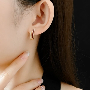 Gros plan de boucles d'oreilles dorées avec émail rouge et zircons portées par un mannequin
