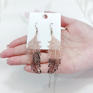 Detailed view of hollow carved feather earrings in rose gold finish on a display card