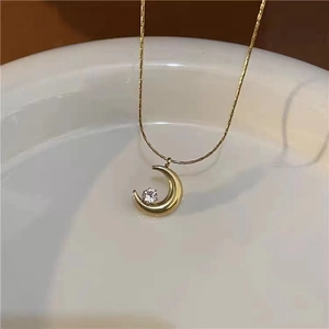 Minimalist moon pendant necklace with crystal in gold finish on white ceramic display