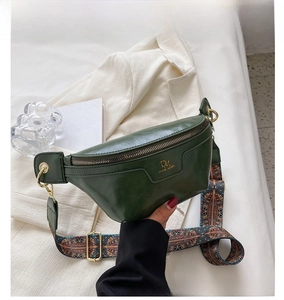 Detail of dark green crescent chest bag with colorful woven strap and gold DM logo