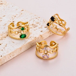Detailed macro view of three layered gold rings featuring green, black and pink gemstones