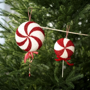 Close-up of red and white spiral lollipop Christmas ornaments with glitter on pine tree
