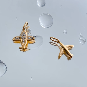 Detail of gold aircraft pendants with cubic zirconia inlay on blue water mirror background