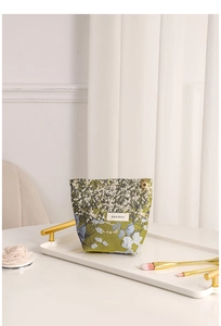 Detail of floral jacquard makeup bag with gold zipper on a decorative white tray