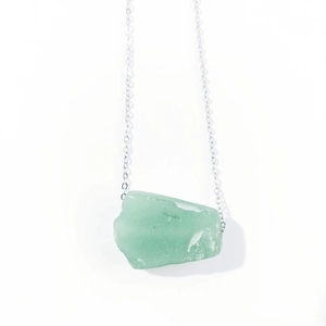 Macro shot of irregular pale green raw crystal pendant on silver link chain necklace