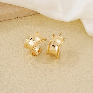 Macro shot of wavy golden irregular geometric earrings on a natural stone surface
