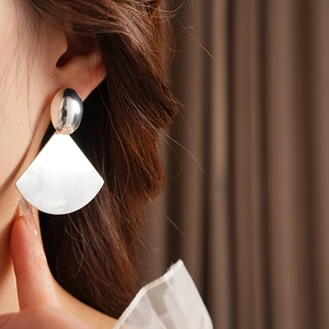 Close-up of geometric fan-shaped brushed metal earrings worn on ear with textured detail