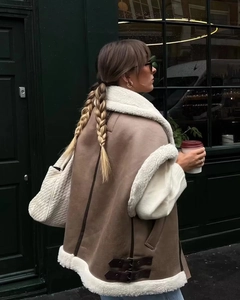 Detail of brown faux shearling vest with cream wool trim and woven shoulder bag