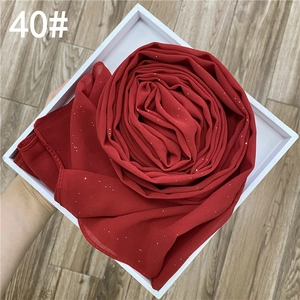 Détail d'un châle en mousseline rouge avec paillettes dorées dans sa boîte cadeau