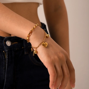 Détail d'un bracelet superposé en acier doré 18 carats avec breloques cœur et bille au poignet
