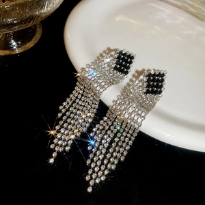 Macro shot of silver diamond tassel earrings on a white plate with black background