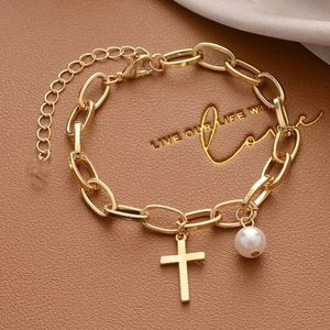 Gold chain bracelet with heart pearl and cross pendant on textured brown leather