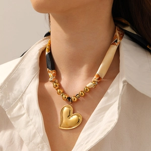 Close-up of golden heart pendant on vintage printed silk ribbon and metal bead necklace