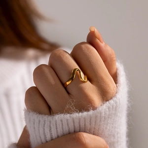 Close-up of minimalist irregular gold wave ring worn by a model with soft lighting