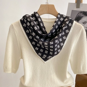 Elegant black and white geometric print silk scarf displayed on a white knit top