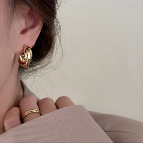 Détail de clips d'oreilles géométriques torsadés dorés portés par un mannequin