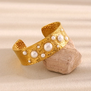 Detail of wide 18K gold-plated hammered cuff bracelet with pearls on a natural stone