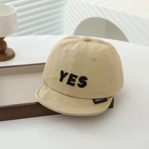 Detail of beige cotton baby baseball cap featuring black YES embroidery on soft fabric