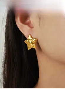 Détail des boucles d'oreilles étoile dorées vintage avec texture martelée sur modèle