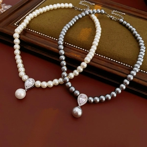 Detail of white and gray pearl necklaces with zircon water drop pendants in a wooden tray
