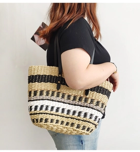 Side view of model carrying a striped straw tote bag with black leather handles
