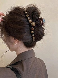 Dettaglio di grande pinza per capelli color ambra con perline su capelli castani