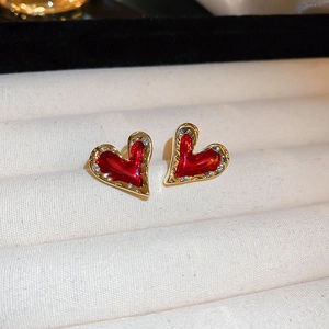 Close-up of red heart earrings with golden diamond borders in a beige jewelry box