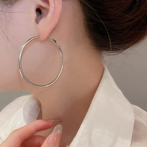 Close-up of a large polished silver hoop earring worn by a model in a minimalist style