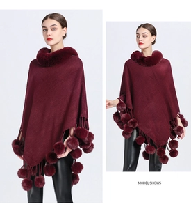 Detail of burgundy knit poncho featuring a faux fur collar and pom-pom tassel hemline