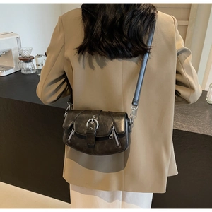 Detail of vintage black leather saddle bag with silver buckles and side zippers on a model