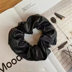 Elegant black faux leather scrunchie with pleated design on a minimalist background