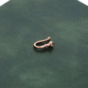 U-shaped rose gold non-piercing nose ring with sparkling diamonds on green surface