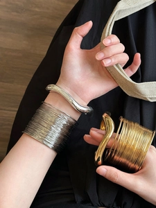 Close-up of stacked gold and silver irregular wavy metal cuff bracelets on a wrist