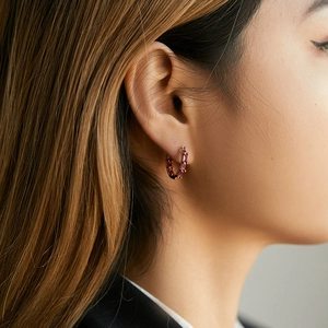 Close-up of 18K gold hoop earrings with rectangular pink zircon stones worn on ear