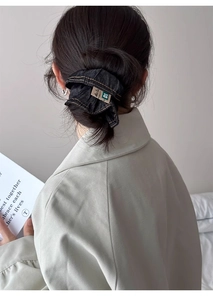 Detail of a high-quality dark denim scrunchie with white stitching on a female hairstyle