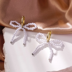 Macro shot of gold hoop earrings with white faux pearl bow charms on champagne satin