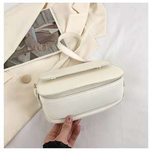 Close-up of minimalist cream leather saddle bag with gold buckle and smooth stitching