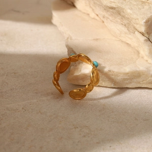 Detail of bohemian gold ring with natural turquoise beads on a natural stone surface