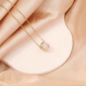 Close-up of square zircon pendant on gold chain against elegant champagne silk background