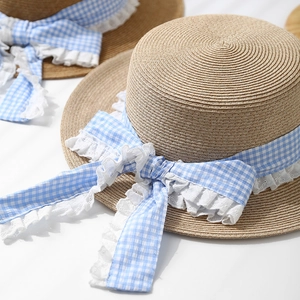 Detail of flat top straw hat featuring a blue gingham ribbon and white lace trim edge