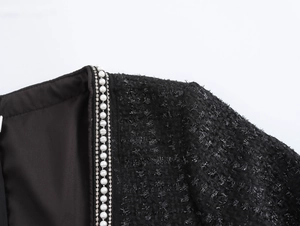 Detail eines schwarzen Tweedkleides mit elegantem Perlen- und Strassbesatz am Ausschnitt