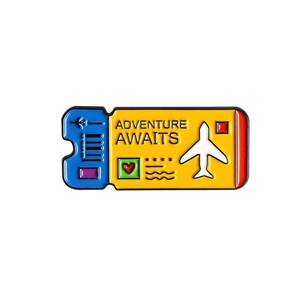 Detail of colorful enamel boarding pass brooch with Adventure Awaits lettering for travel