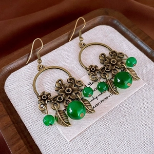 Détail de boucles d'oreilles en bronze vintage avec perles vertes et charms feuilles