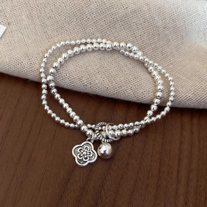 Detail showing double-layered silver beaded bracelet with hollow flower and bell pendants