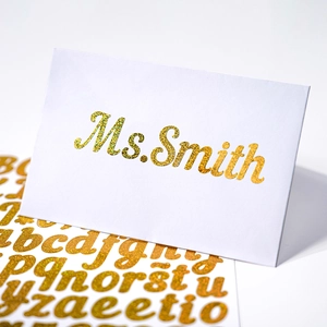 Detail of gold glitter letter stickers showing 'Ms. Smith' on a white gift card