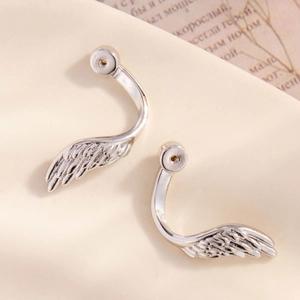 Polished silver wing-shaped stud earrings on vintage book page with a retro aesthetic