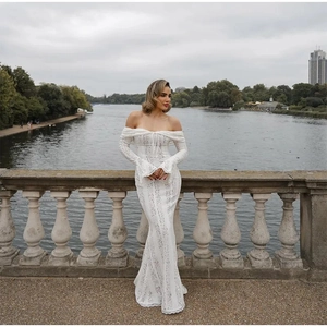 Elegant white lace off-shoulder dress with bell sleeves and floor-length skirt on a bridge