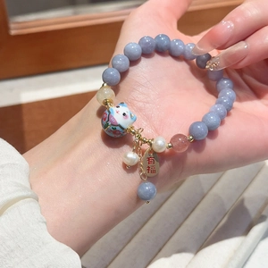 Macro del bracciale con perline viola, ciondolo Maneki-neko e medaglietta portafortuna