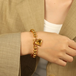Elegant gold beaded bracelet featuring a polished heart pendant on a model's wrist